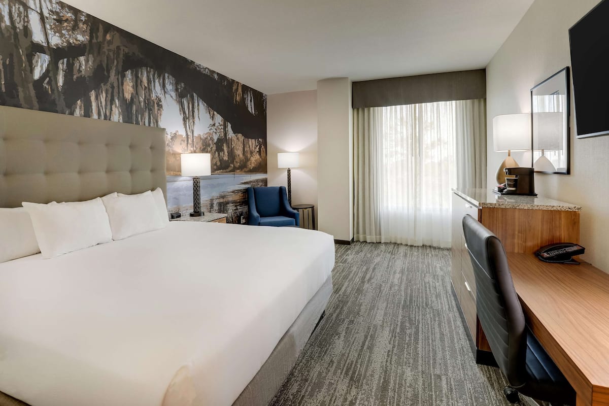 A hotel room with a large bed, a desk, a chair, a lamp, and a painting on the wall.