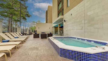 A rooftop pool area with lounge chairs and a hot tub.