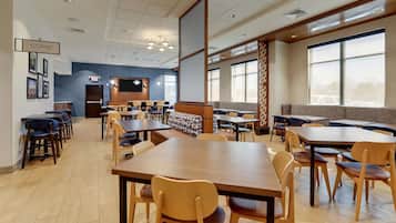 A spacious indoor area with multiple tables and chairs, a coffee station, and large windows providing natural light.