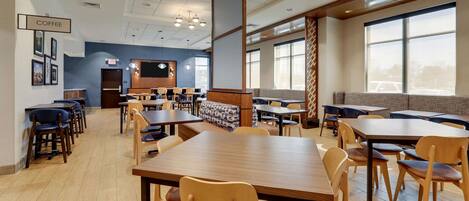 A spacious indoor area with multiple tables and chairs, a coffee station, and large windows providing natural light.