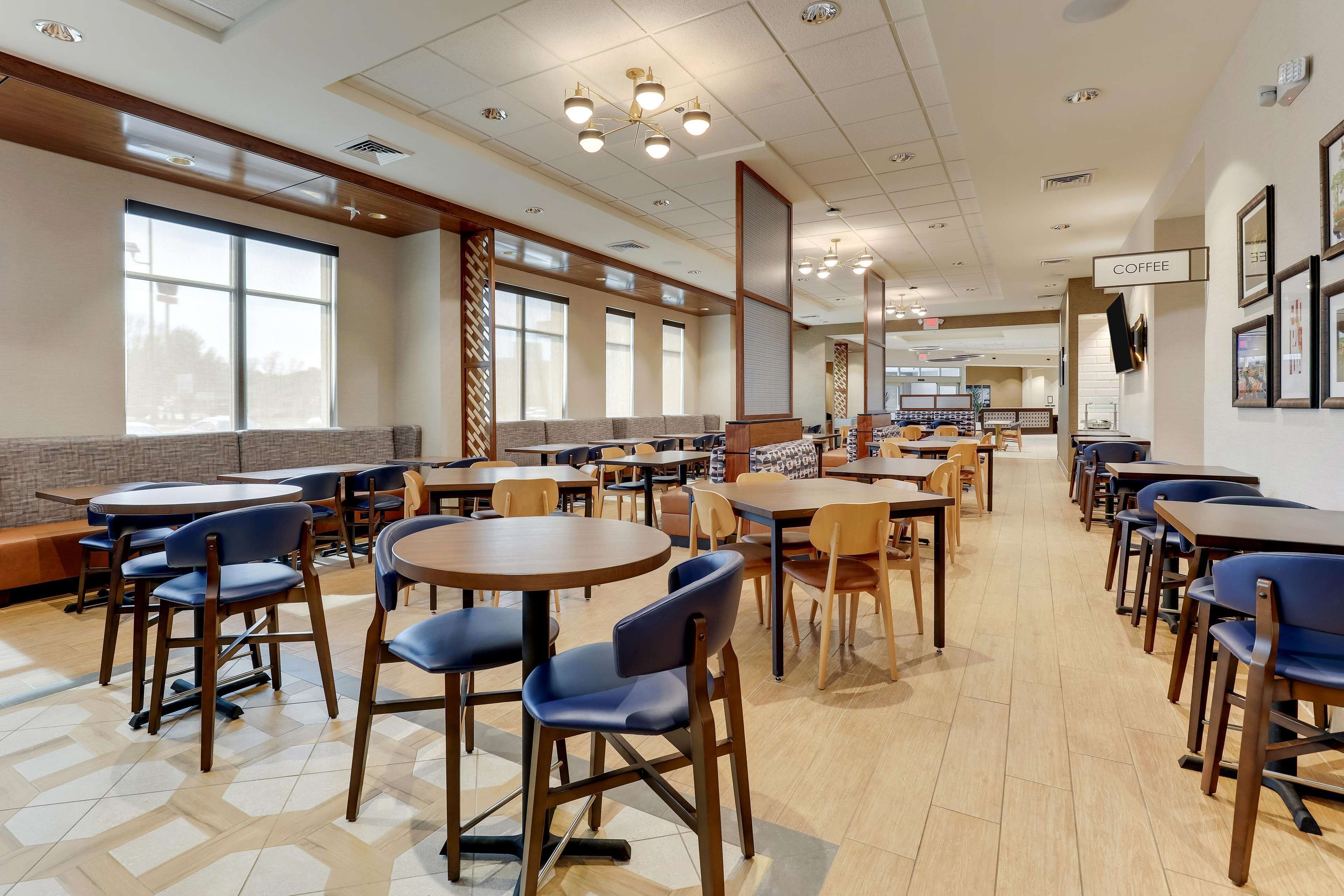 Una amplia cafetería con varias mesas y sillas, ventanas grandes y una estación de café.