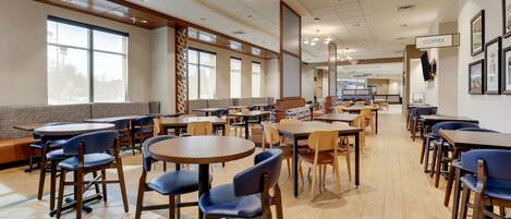Una amplia cafetería con varias mesas y sillas, ventanas grandes y una estación de café.