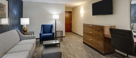 A hotel room with a sofa, armchair, desk, and TV.