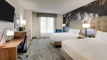 A hotel room with two beds, a desk, a chair, a TV, and a large window with curtains.