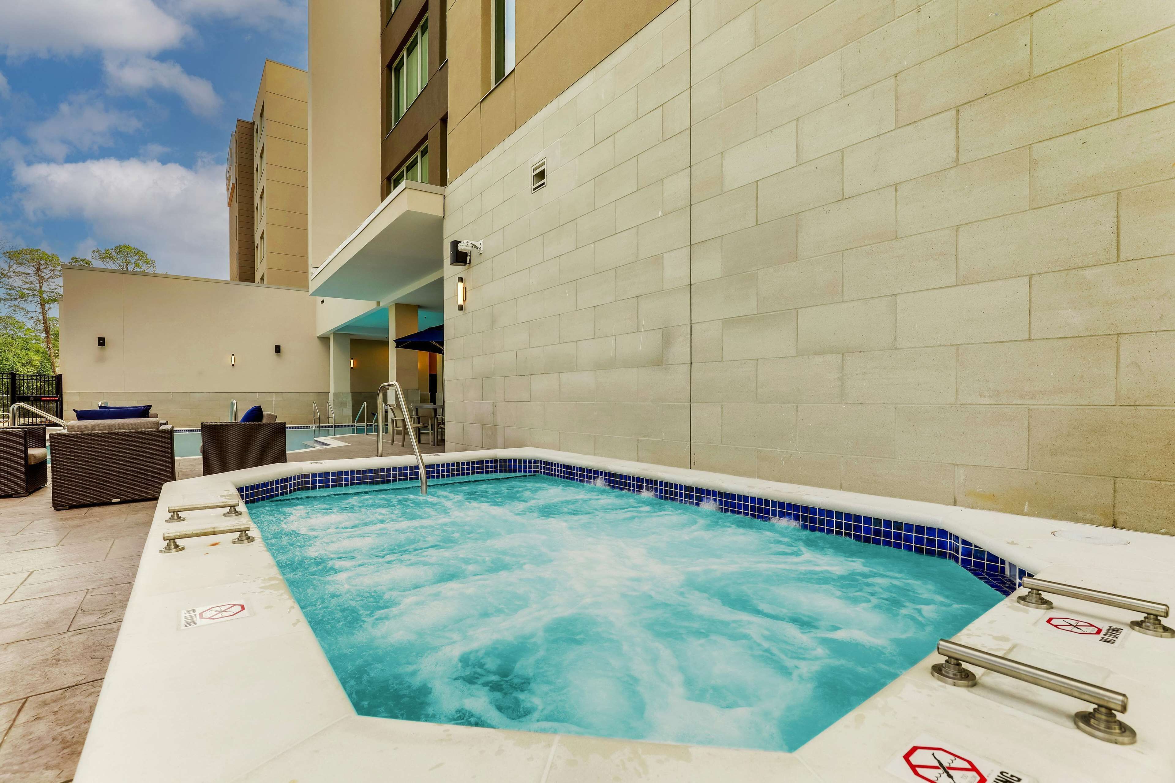 A hot tub with a blue tiled edge, surrounded by a beige tiled wall and a clear sky.
