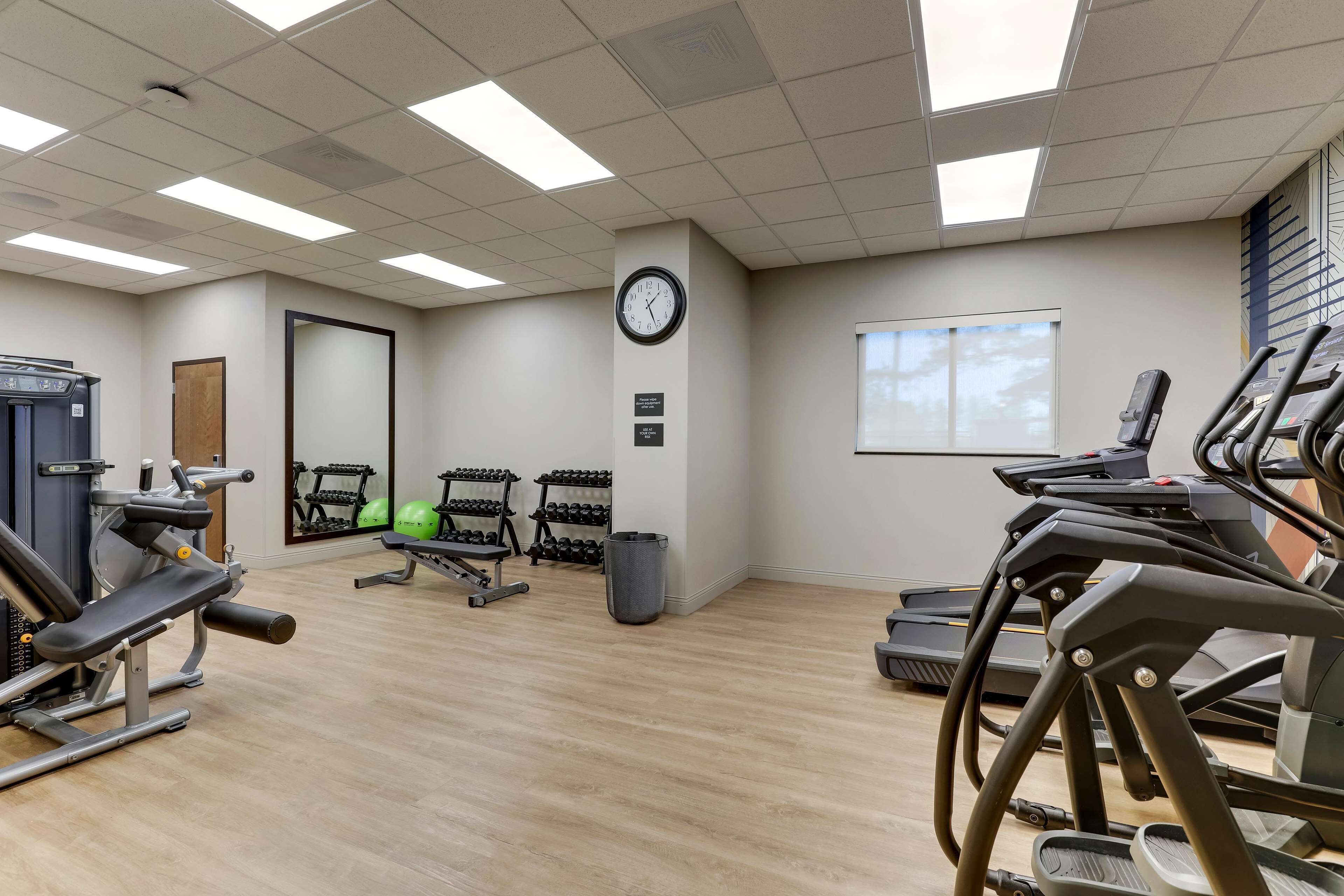 Een sportschool met fitnessapparatuur, een klok en een raam.