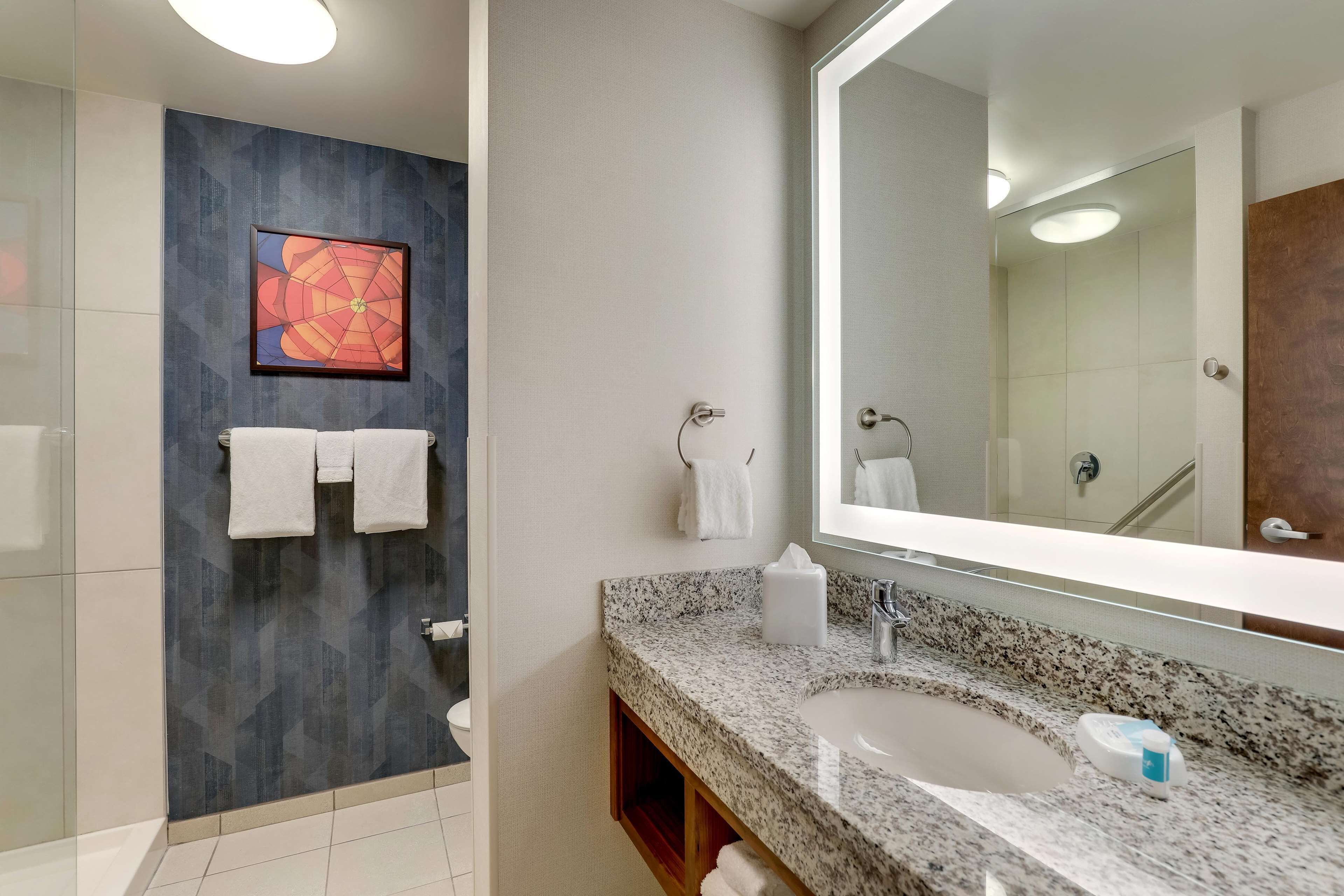 A modern bathroom with a granite countertop, a large mirror, and a wall-mounted towel rack.