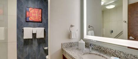 A modern bathroom with a granite countertop, a large mirror, and a wall-mounted towel rack.