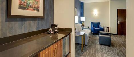 A hotel room with a wooden cabinet, a framed picture on the wall, a seating area with a blue chair and a small table, and a carpeted floor.