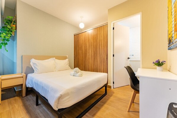 Relax in a serene space with a neatly made bed, desk, and comfortable seating area.