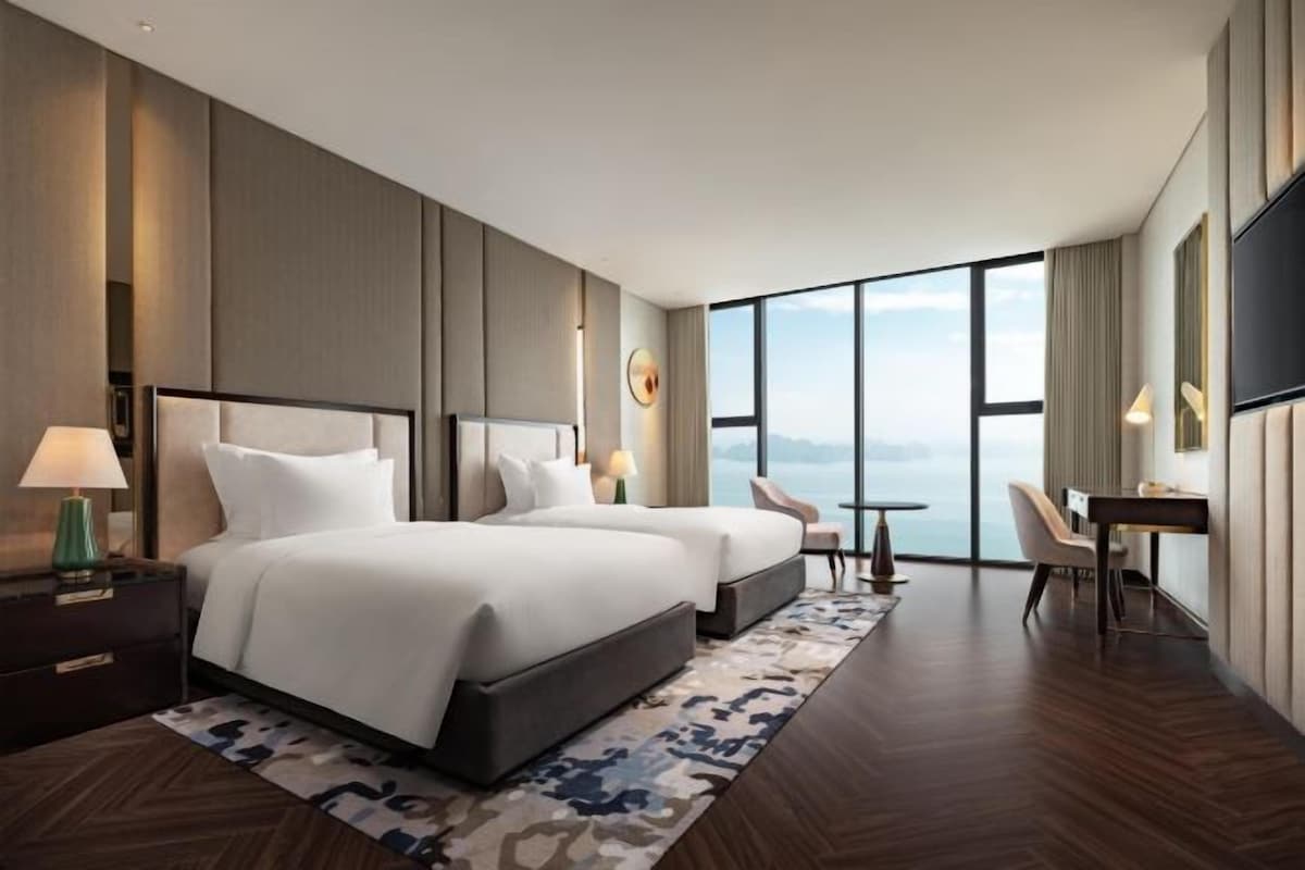 A modern hotel room with a large bed, a desk, and a view of the city.