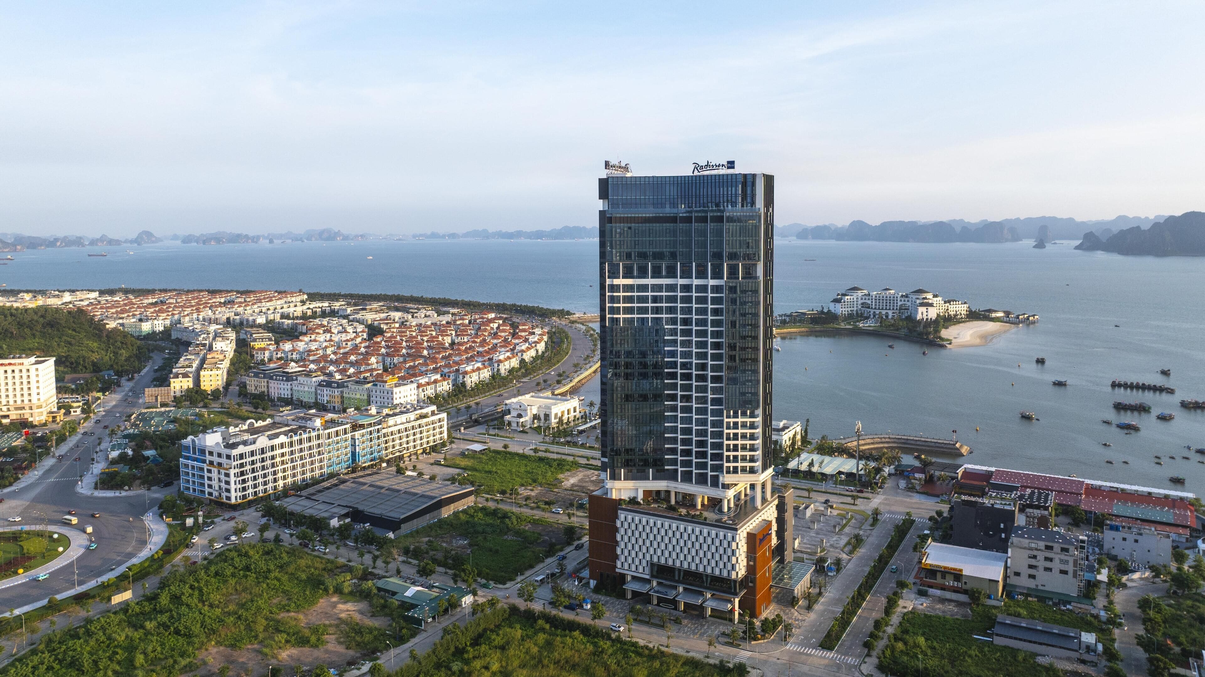 A high-rise building with a modern glass facade, situated near a waterfront with a marina and residential buildings.