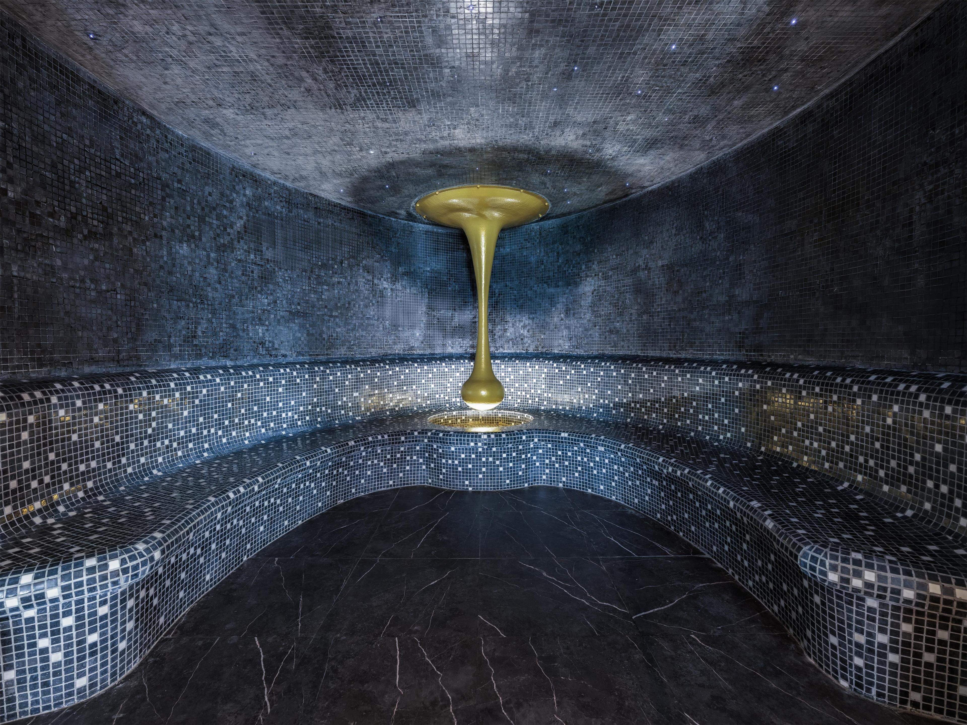 A room with a mosaic-tiled wall and floor, a central column, and a ceiling with a grid pattern.