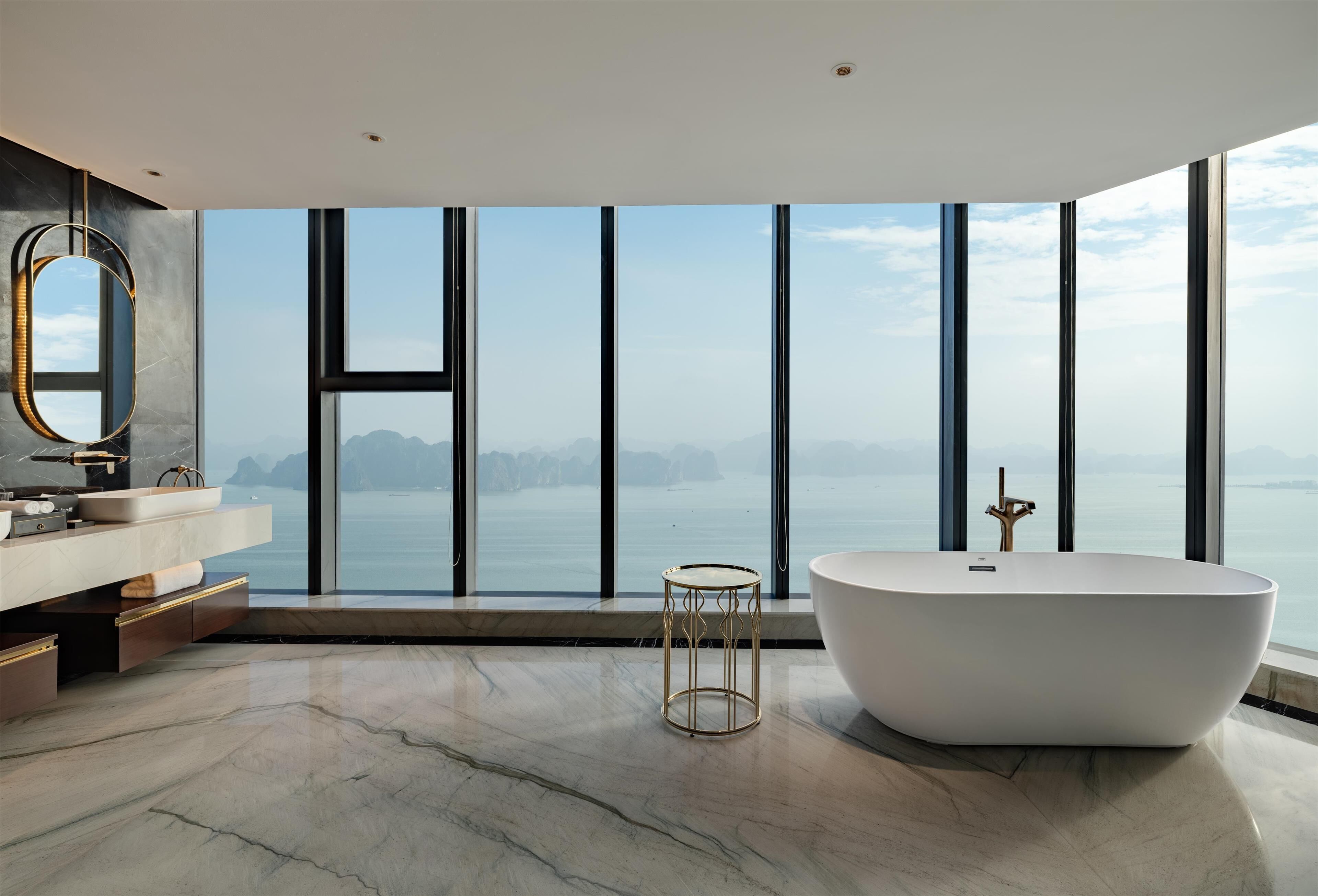 A modern bathroom with a large bathtub, a vanity with a mirror, and a view of the sea.