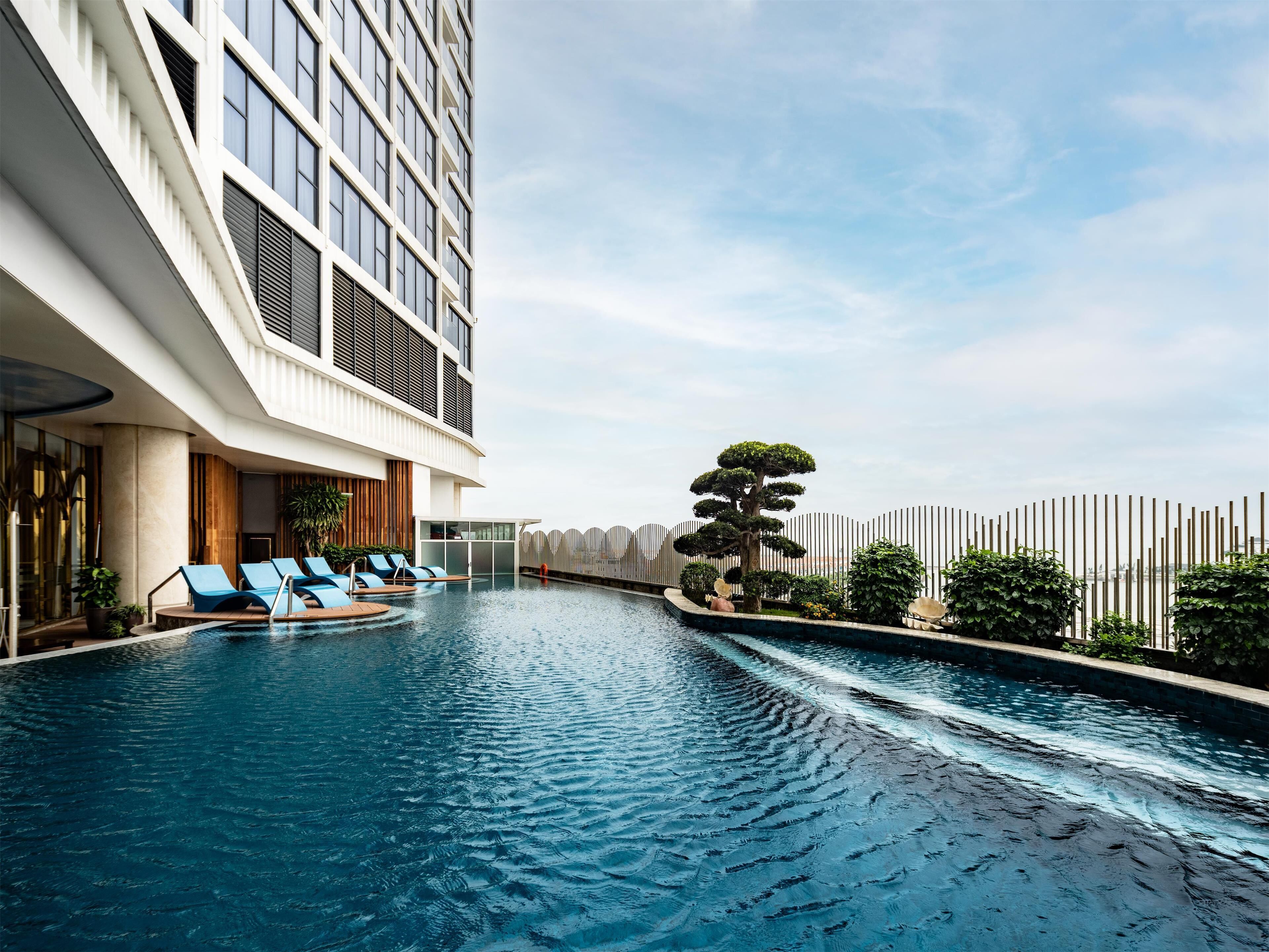 A modern hotel with a rooftop infinity pool, lounge chairs, and a well-maintained garden.
