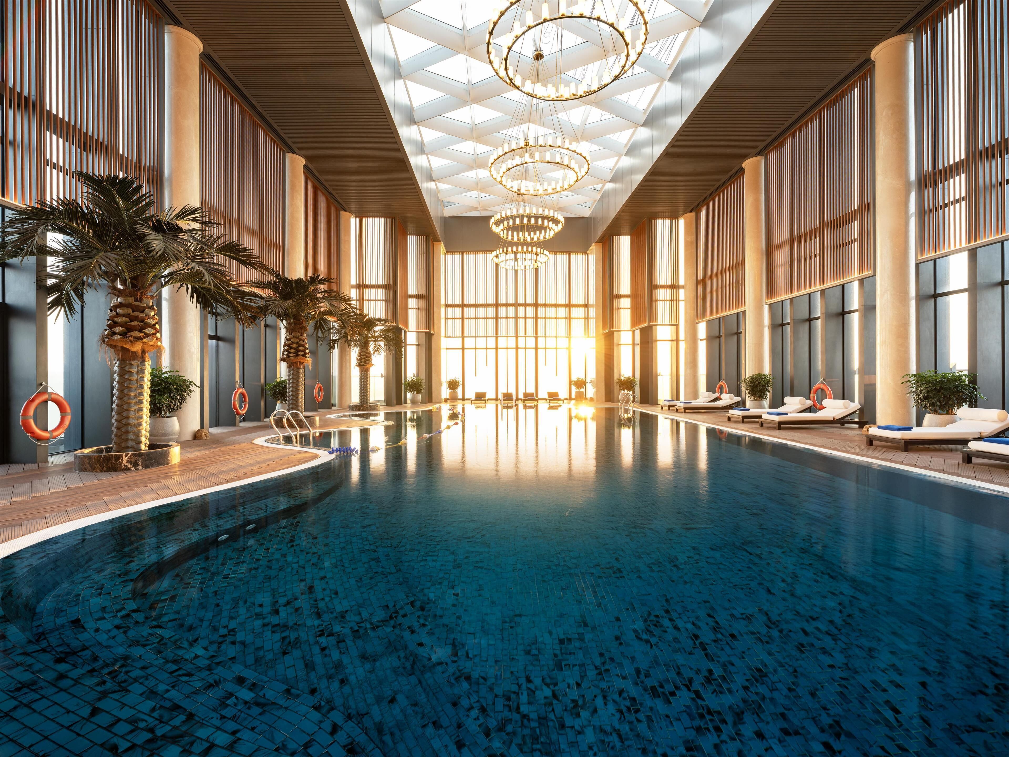 An indoor swimming pool with lounge chairs and palm trees.