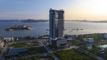 A high-rise hotel with a modern architectural design, situated near a body of water with boats and a distant island.