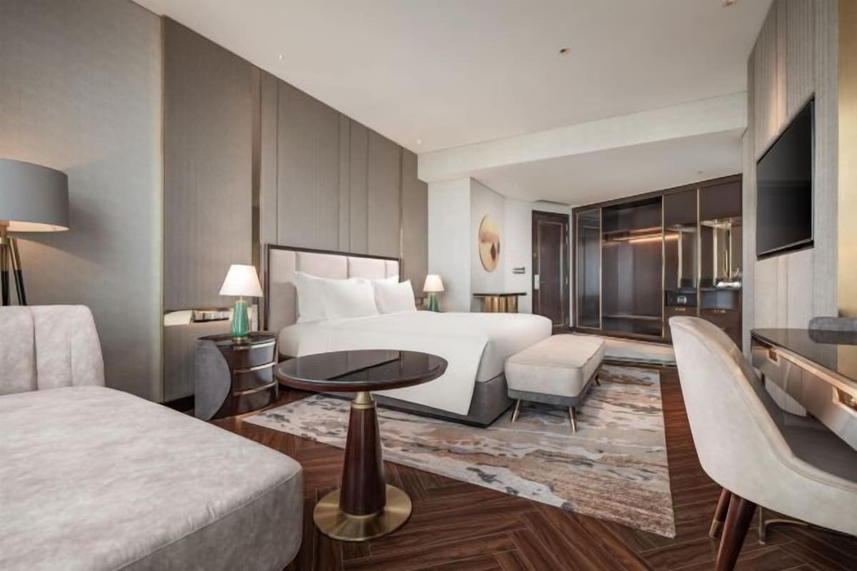 A modern hotel room with a large bed, a desk, a chair, and a television.