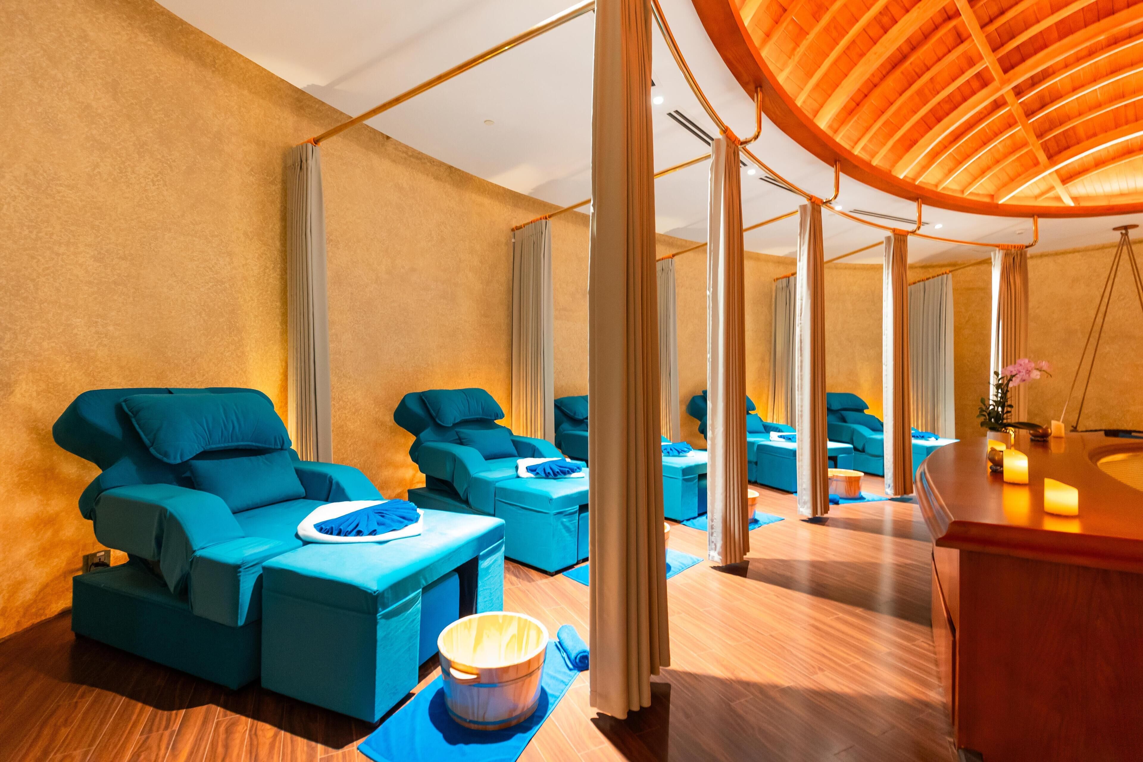Une salle de spa équipée de fauteuils de massage, d’un comptoir d’accueil en bois et d’un plafond incurvé.