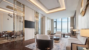 A modern hotel room with a large window, a flat-screen TV, a sofa, a coffee table, and a dining area with a table and chairs. - Radisson Blu Hotel, Ha Long Bay (Bai Chay)