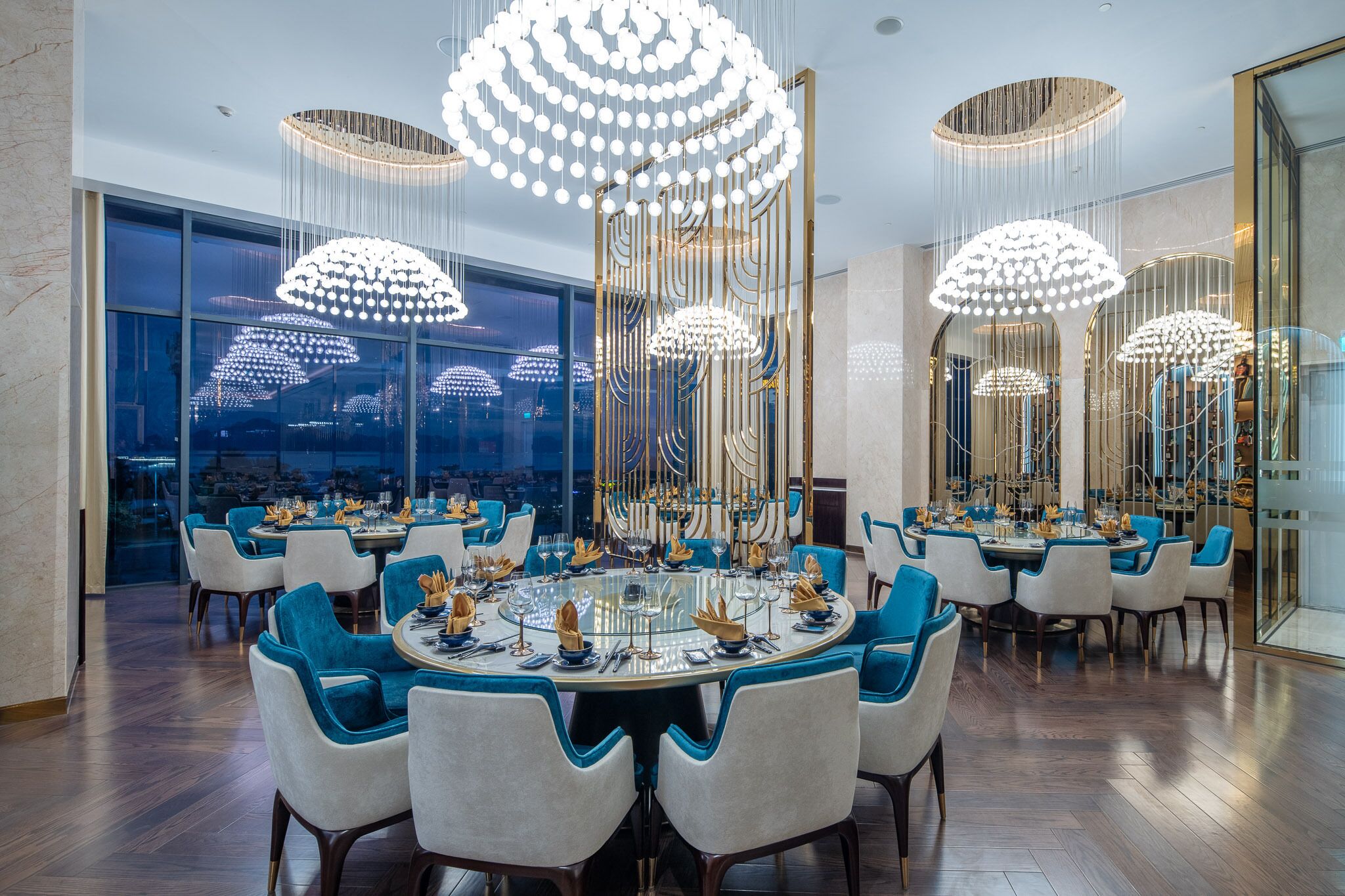 A dining area with round tables, blue and white chairs, and modern chandeliers.