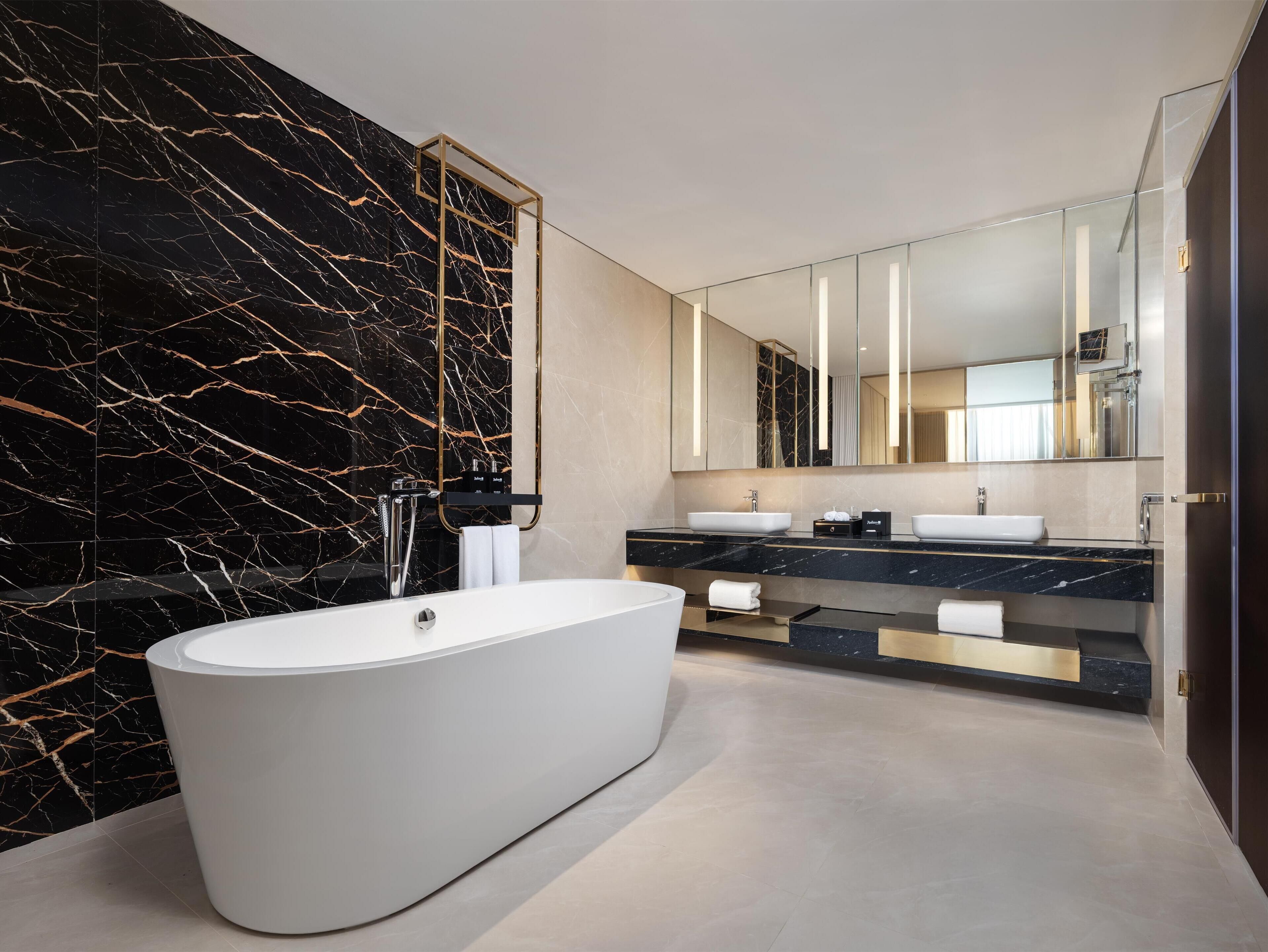 Un baño moderno con una bañera independiente, dos lavamanos y un espejo grande.