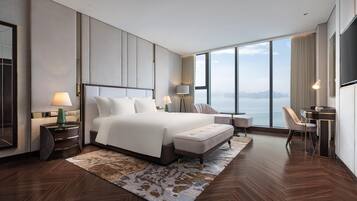 A modern hotel room with a large bed, a desk, and a view of the sea.