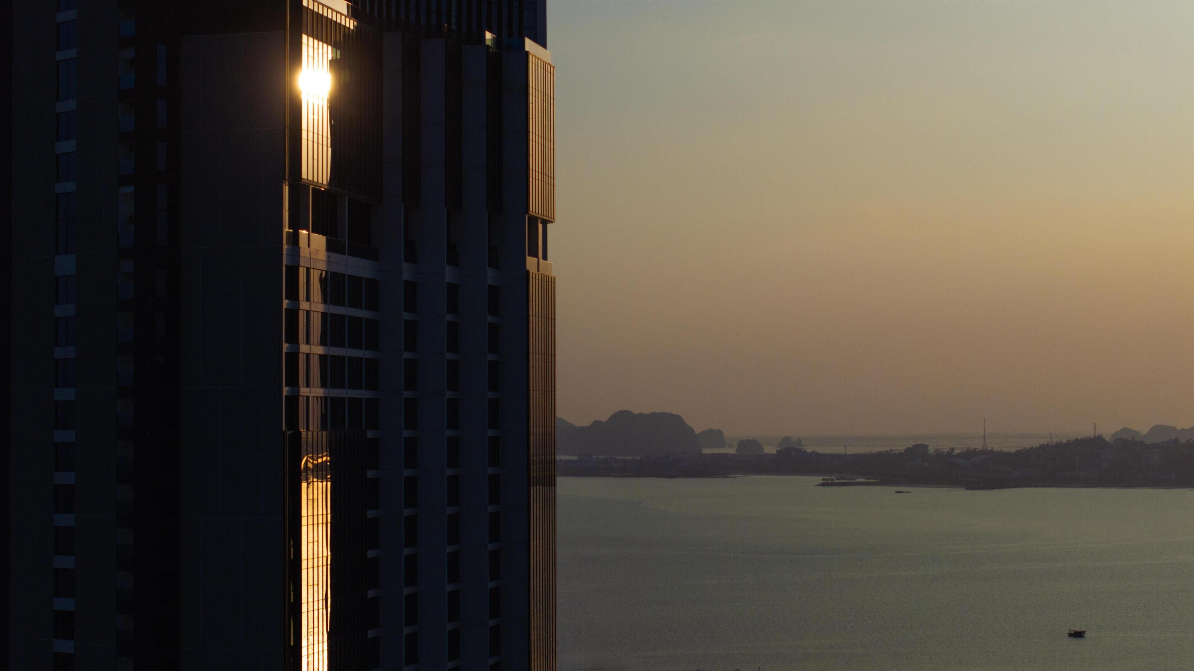 A high-rise building with a view of a calm body of water and distant landforms.