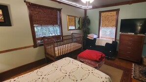 Une chambre avec un berceau, un lit, une télévision et une commode.
