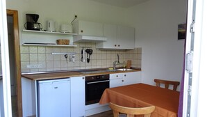 A compact kitchen with white cabinets, a dishwasher, an oven, and a dining table with chairs. - Wohnung 4 a - 1. Etage, 30qm - Eckbalkon (Gstadt am Chiemsee)