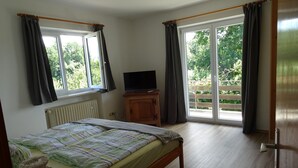 A bedroom with a bed, a television on a wooden cabinet, and a sliding glass door to a balcony. - Wohnung 4 a - 1. Etage, 30qm - Eckbalkon (Gstadt am Chiemsee)