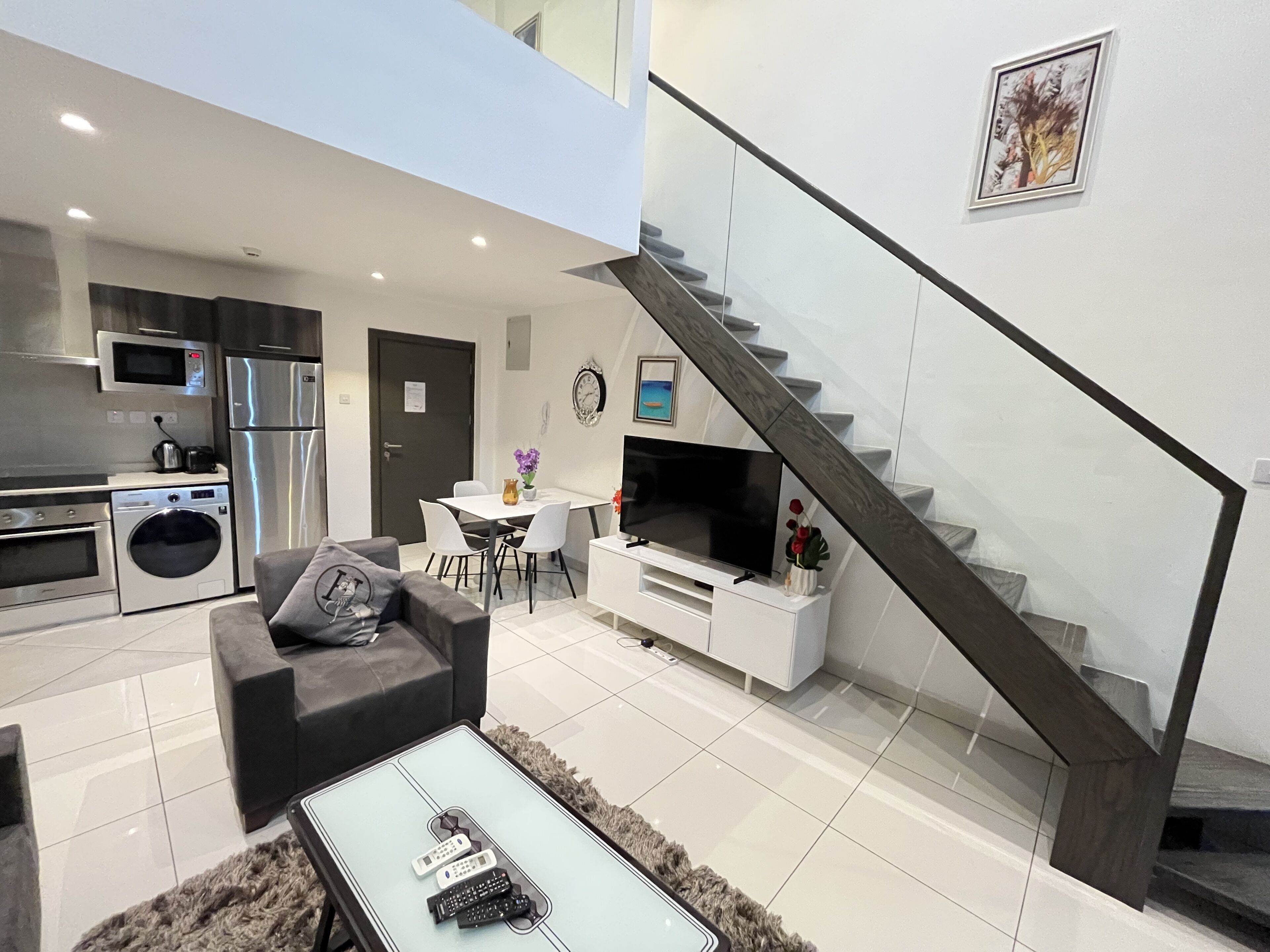 A modern living room with a sofa, coffee table, and TV. There is a staircase leading to an upper level.
