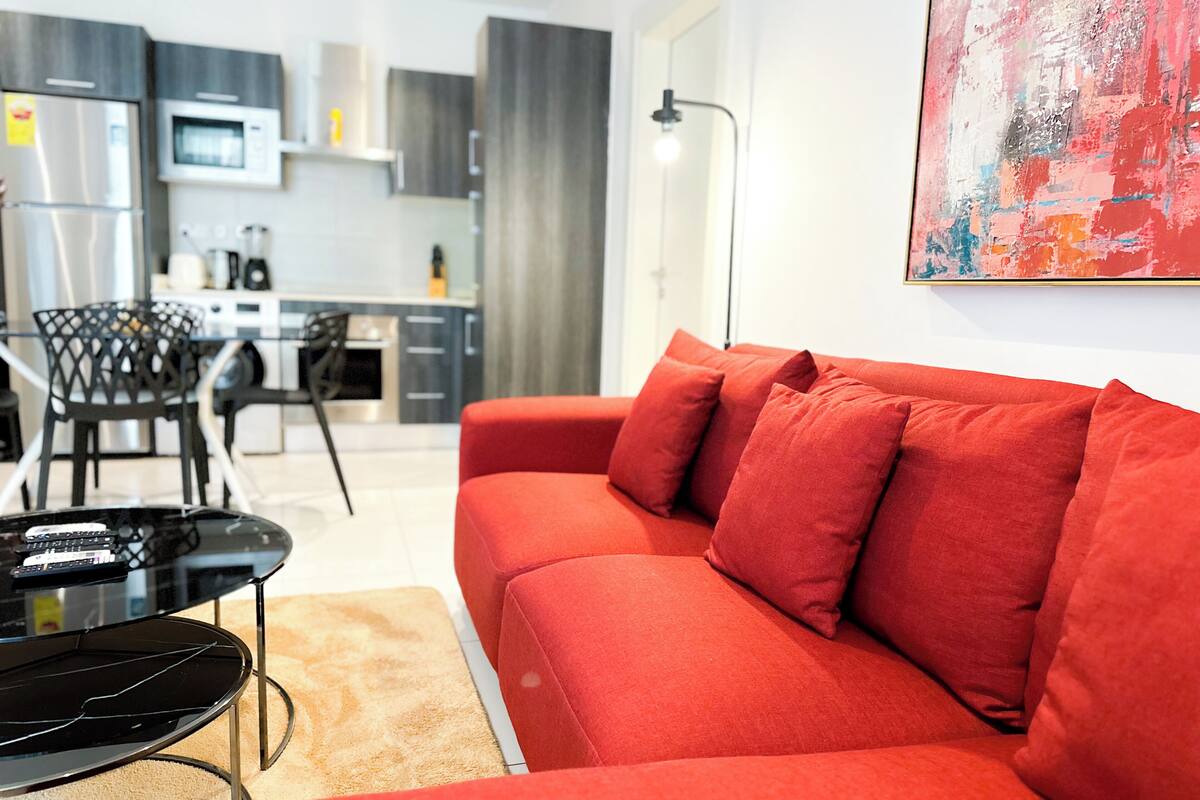 A modern living room with a red sofa, a black coffee table, and a glass dining table.
