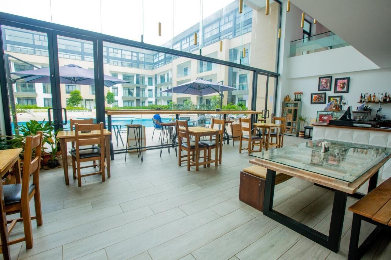 Un comedor interior moderno con mesas y sillas de madera, ventanas amplias y vistas a una piscina y edificios.