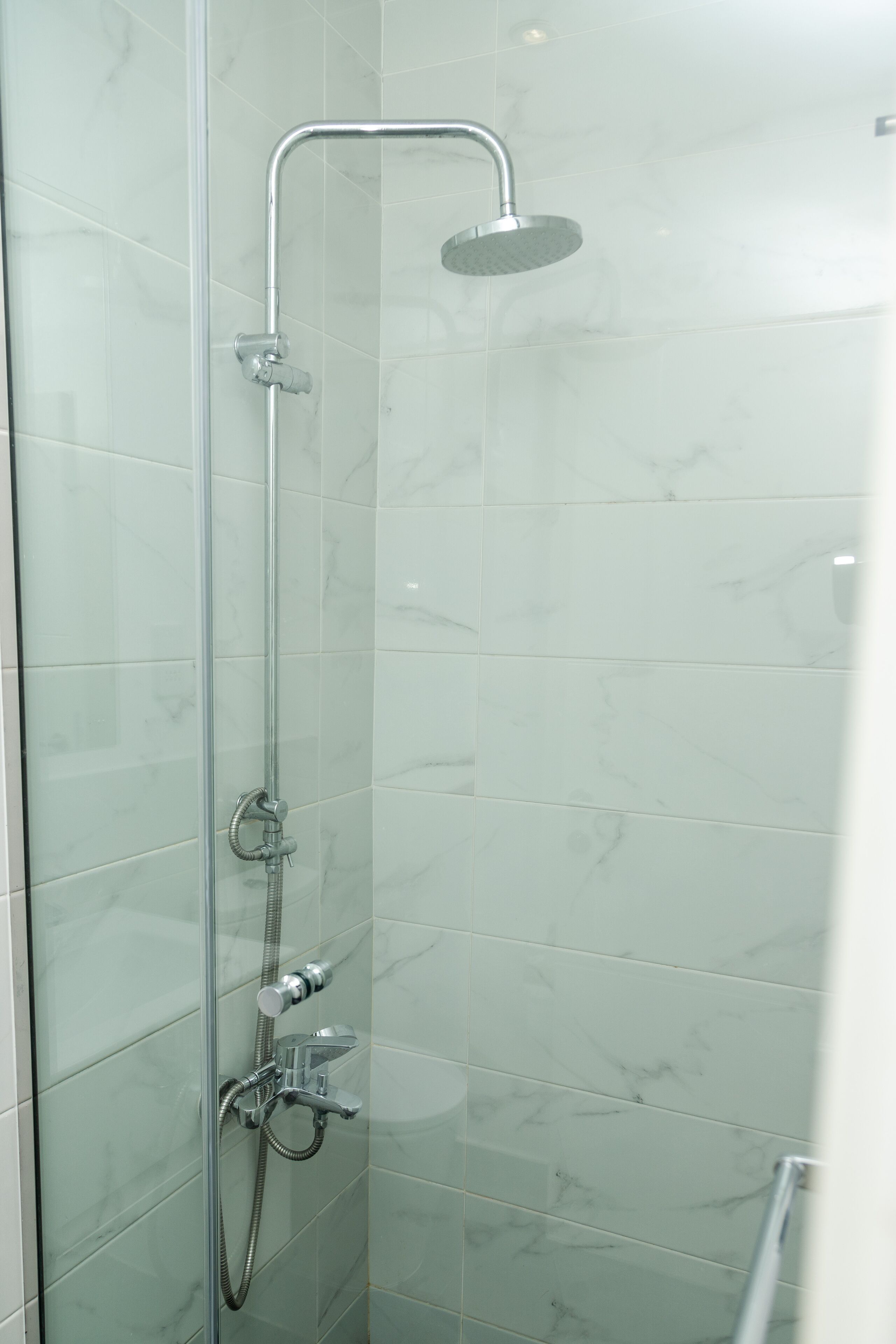 A glass-enclosed shower stall with a handheld showerhead and a wall-mounted faucet.