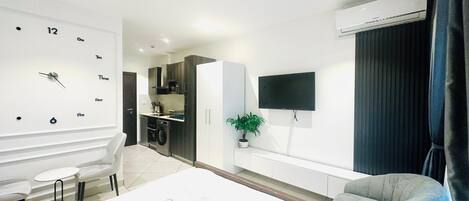 Een moderne hotelkamer met een bed, een zithoek, een kleine kitchenette, een aan de muur bevestigde televisie en een airconditioning.