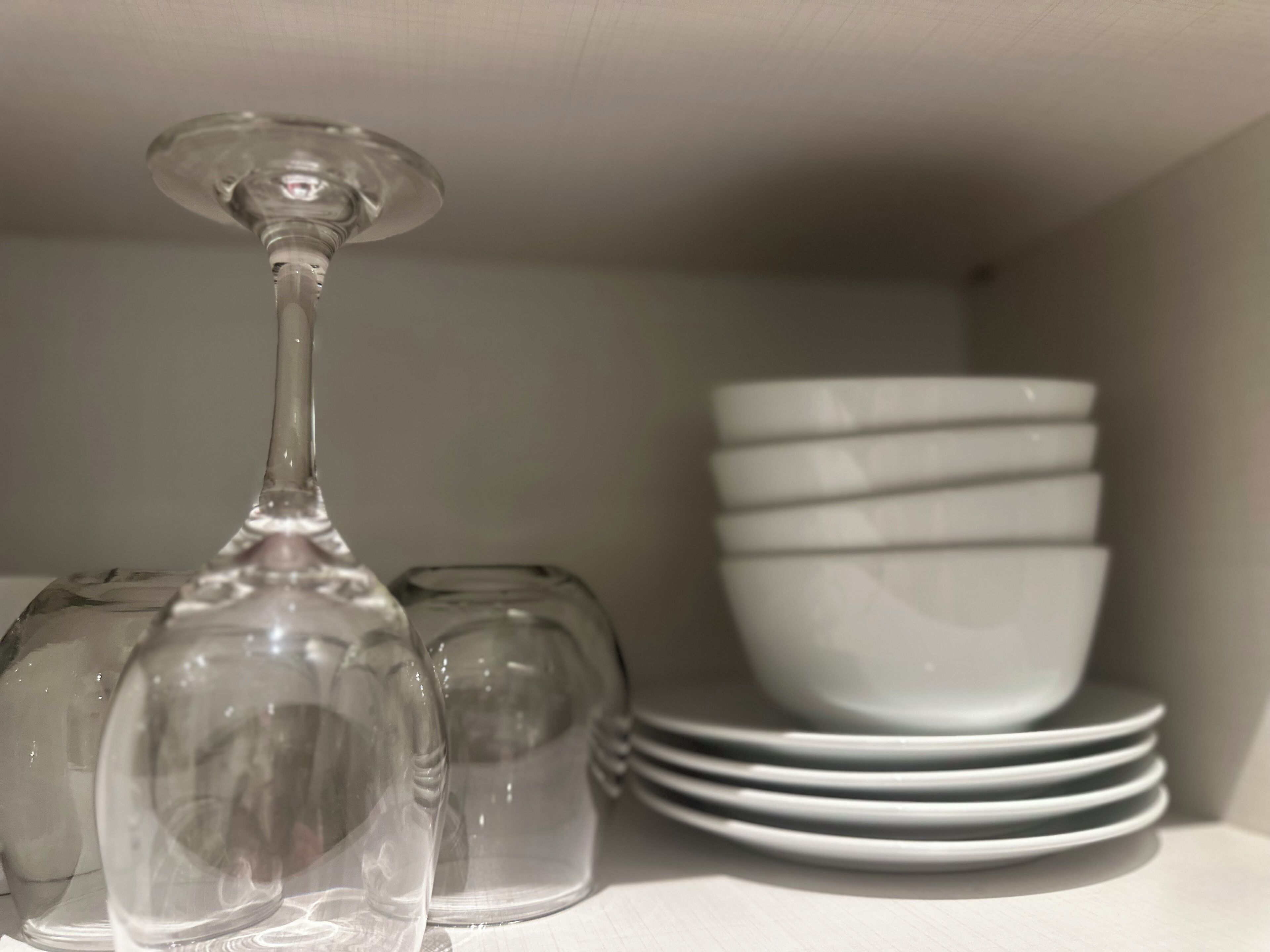 A shelf with a wine glass, a small glass, and stacked white bowls.