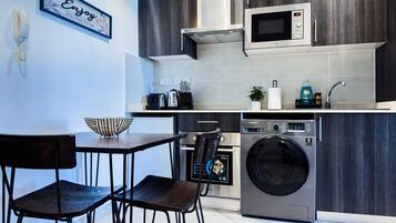 A modern kitchen with dark wood cabinets, a microwave, a washing machine, and a dining area with two chairs.