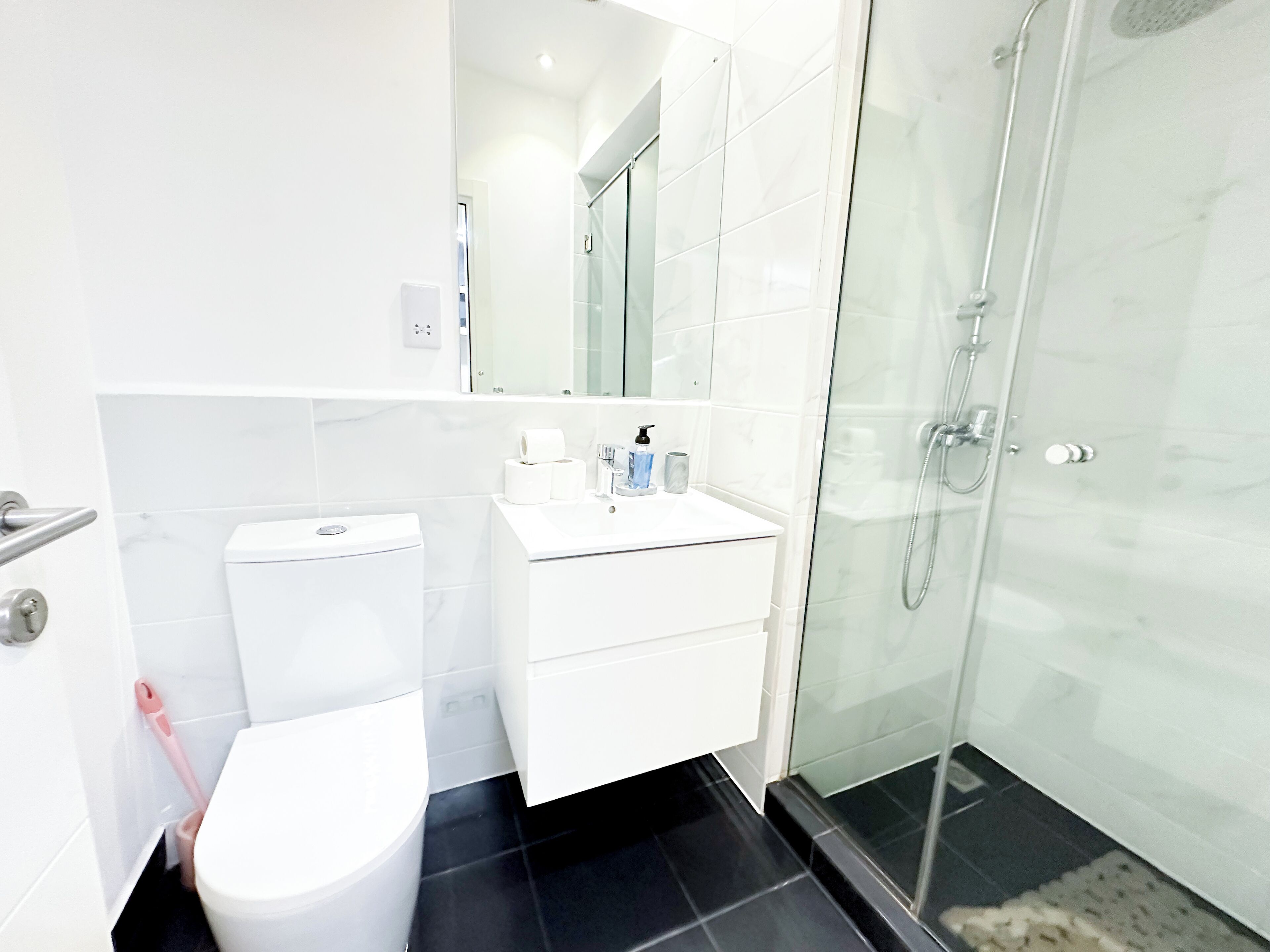 Une salle de bain moderne équipée de toilettes, d’un lavabo et d’une douche à parois de verre.