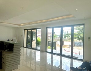 Un hall amplio con una recepción, grandes puertas correderas de vidrio que dan a un espacio exterior, y una decoración interior moderna y elegante.
