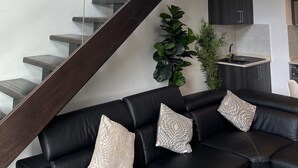 A modern interior with a staircase, a black leather sofa, and a potted plant. - Unique Homes by Embassy Gardens (Accra)