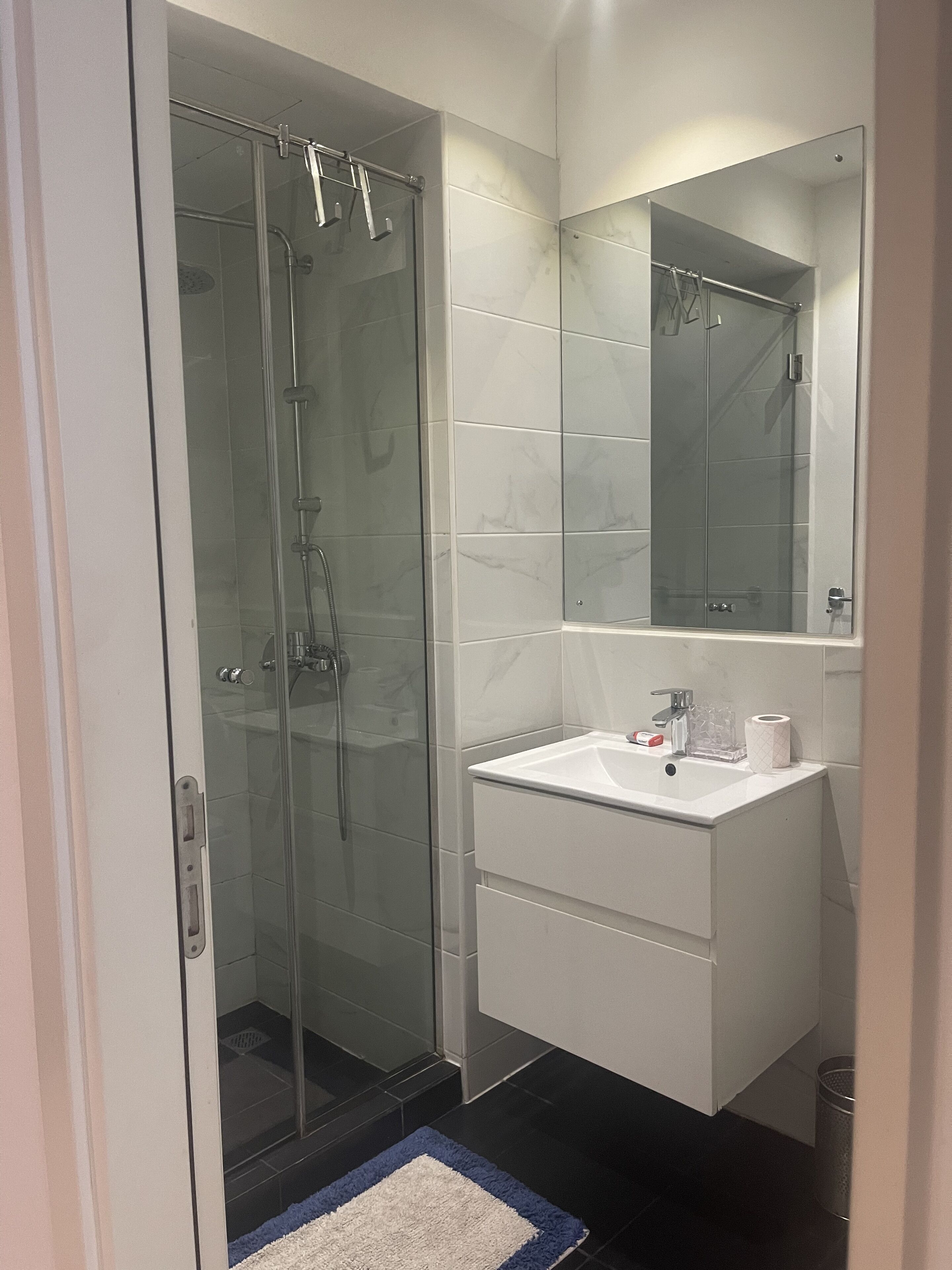 A modern bathroom with a glass-enclosed shower, a white vanity with a mirror, and a black tiled floor.
