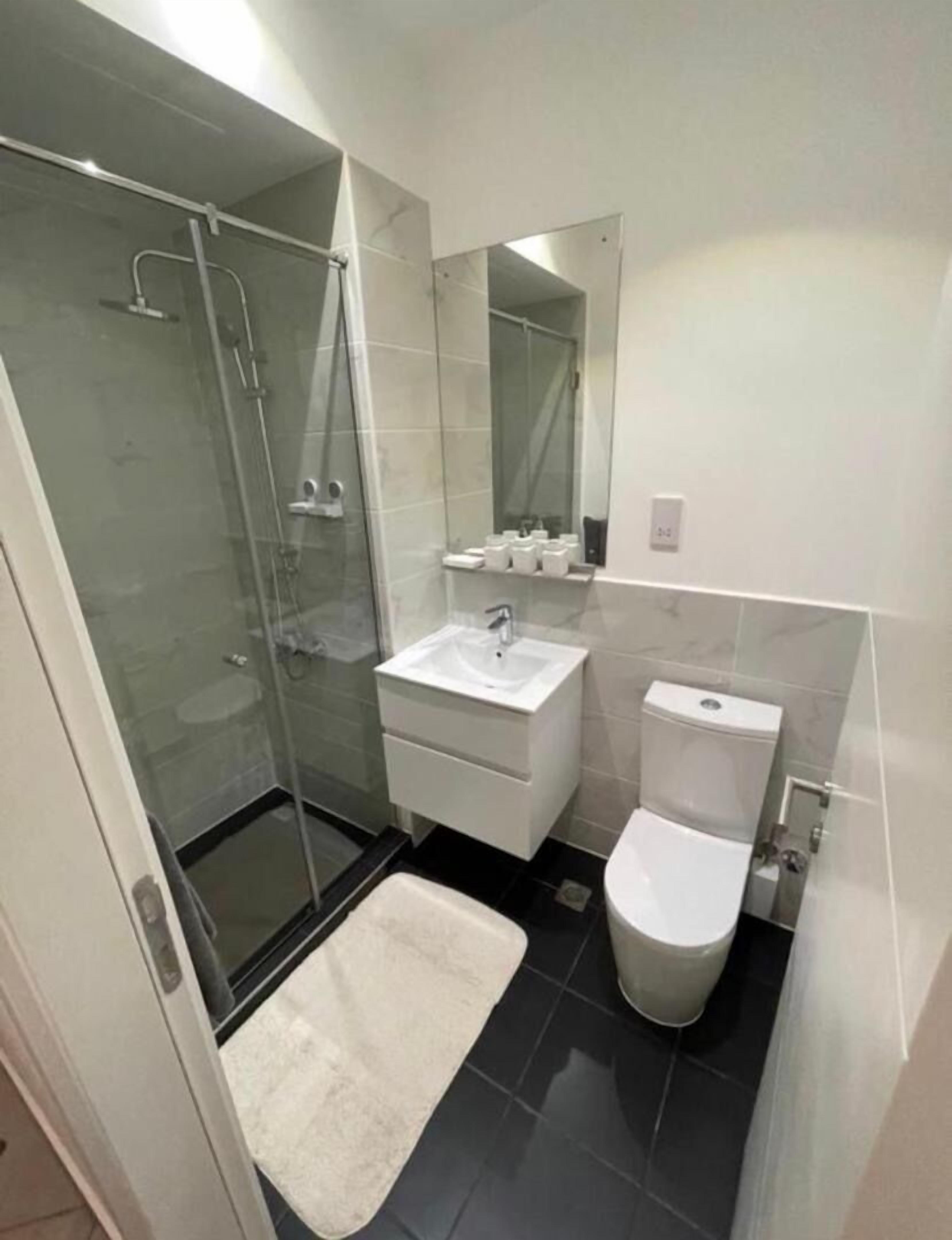 Une petite salle de bain dotée d’une douche à parois de verre, d’un lavabo blanc, de toilettes et d’un miroir au-dessus du lavabo.