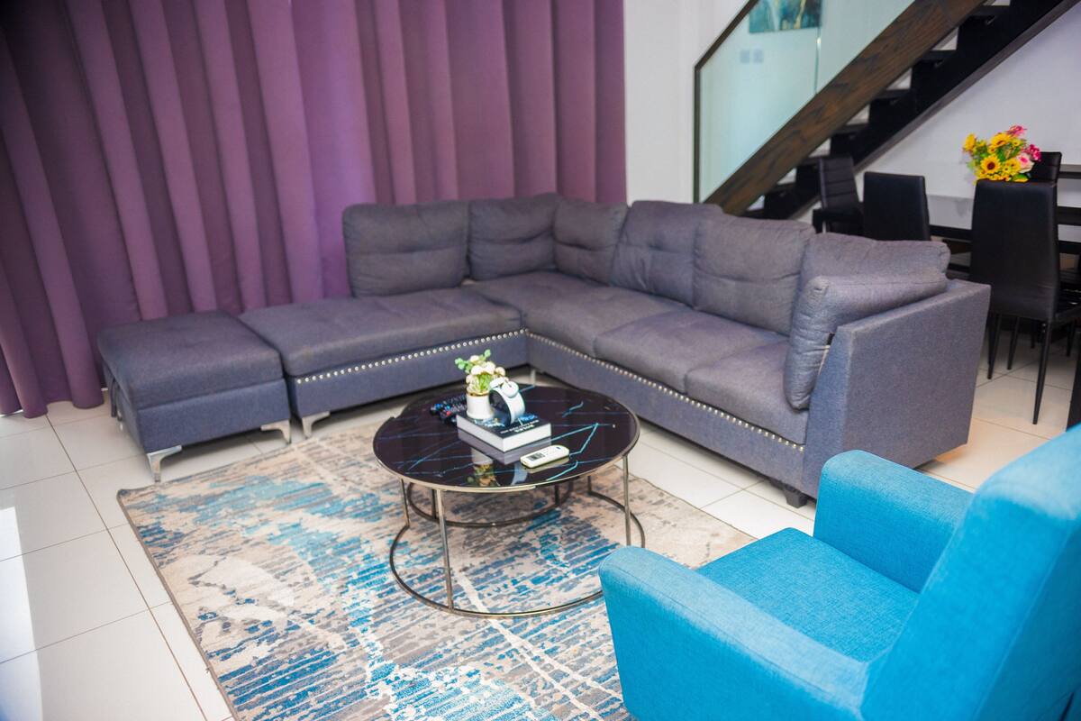 A modern living room with a sectional sofa, a blue armchair, and a coffee table with decorative items.