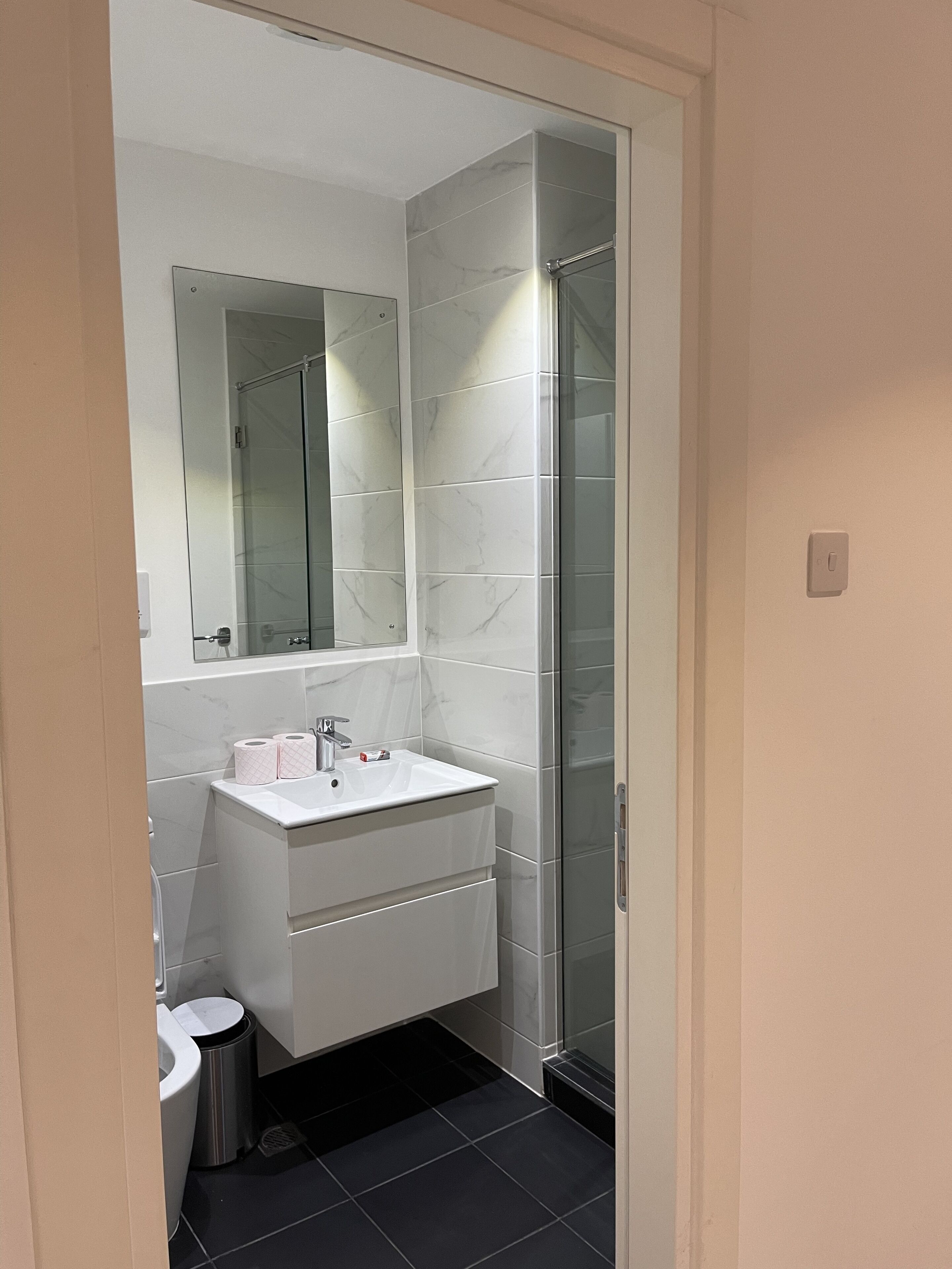 Een moderne badkamer met een wit wastafelmeubel, een glazen douchecabine en een grote spiegel boven de wastafel.