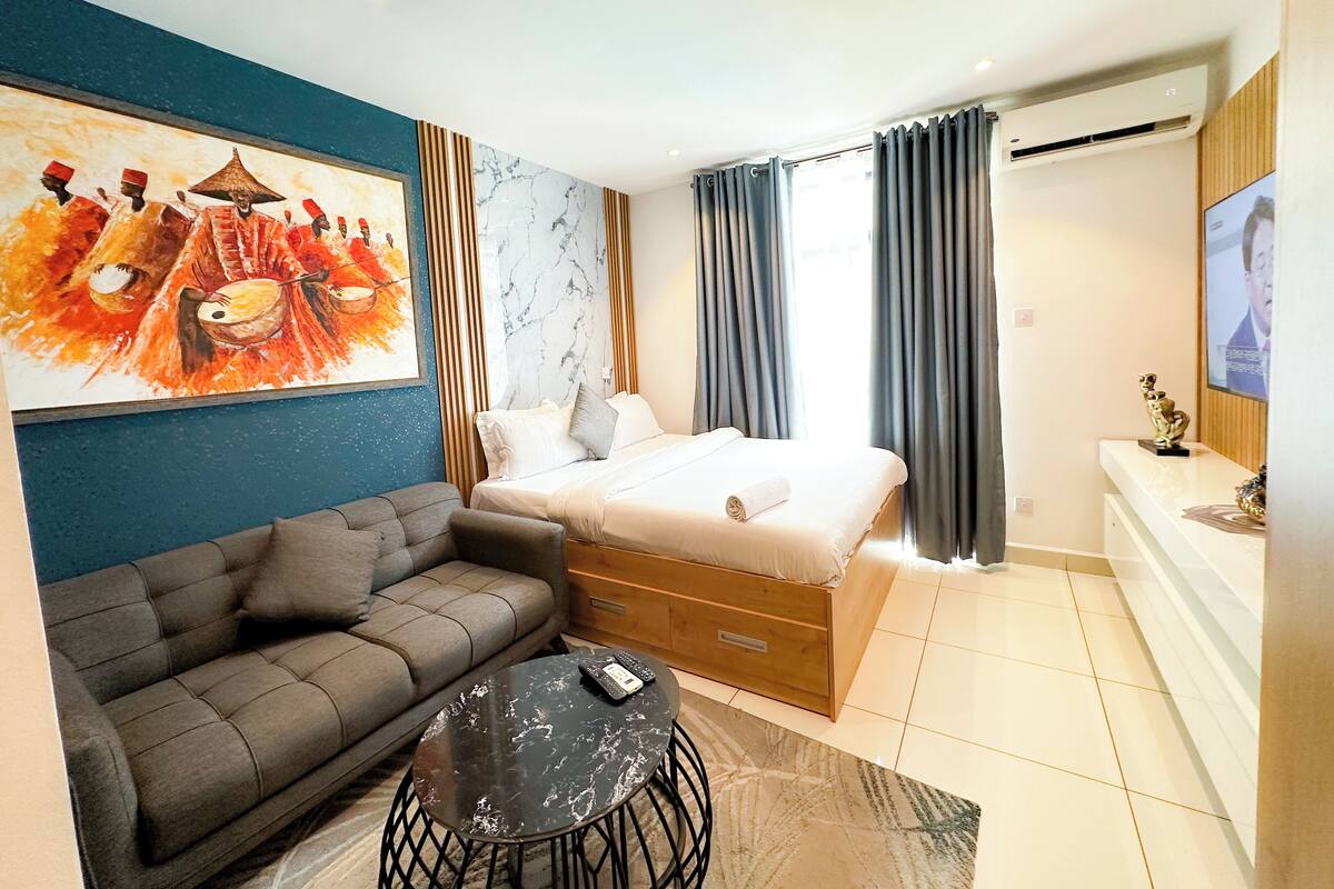 A modern hotel room with a bed, a sofa, a small table, and a painting on the wall.