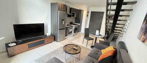 A modern living room with a flat-screen TV, grey sofa, and a coffee table.