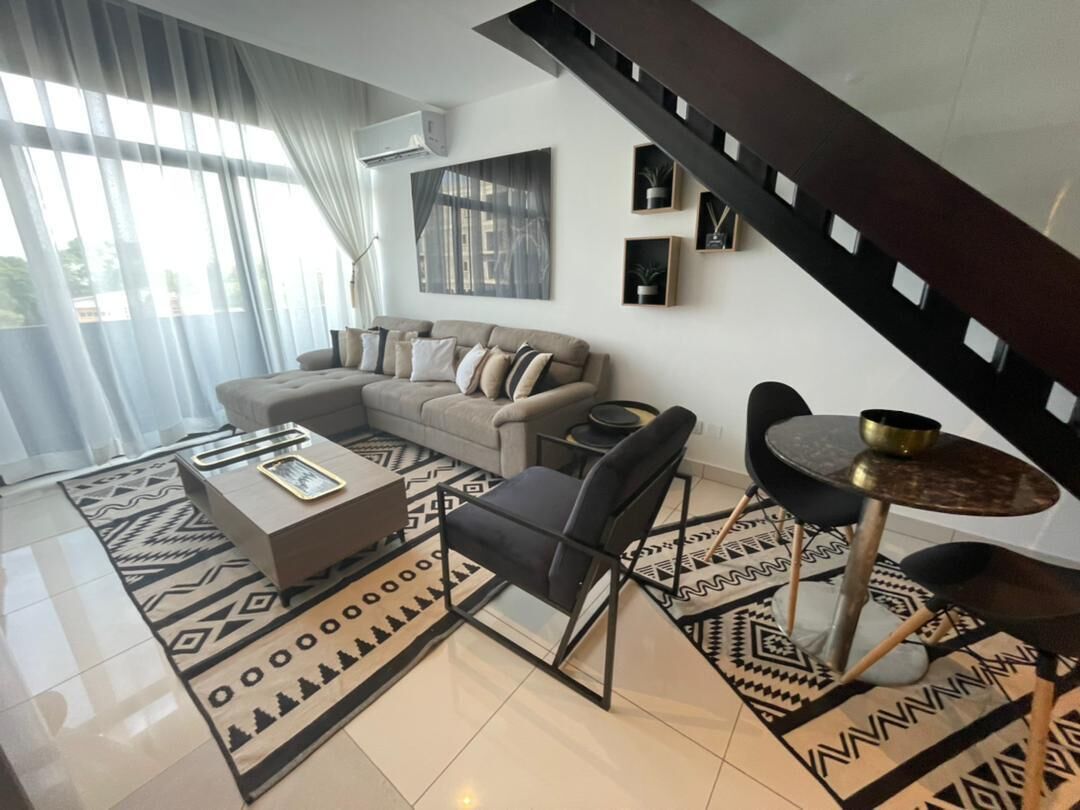 A modern living room with a sofa, coffee table, and chairs, a staircase, and a dining area with a table and chairs.