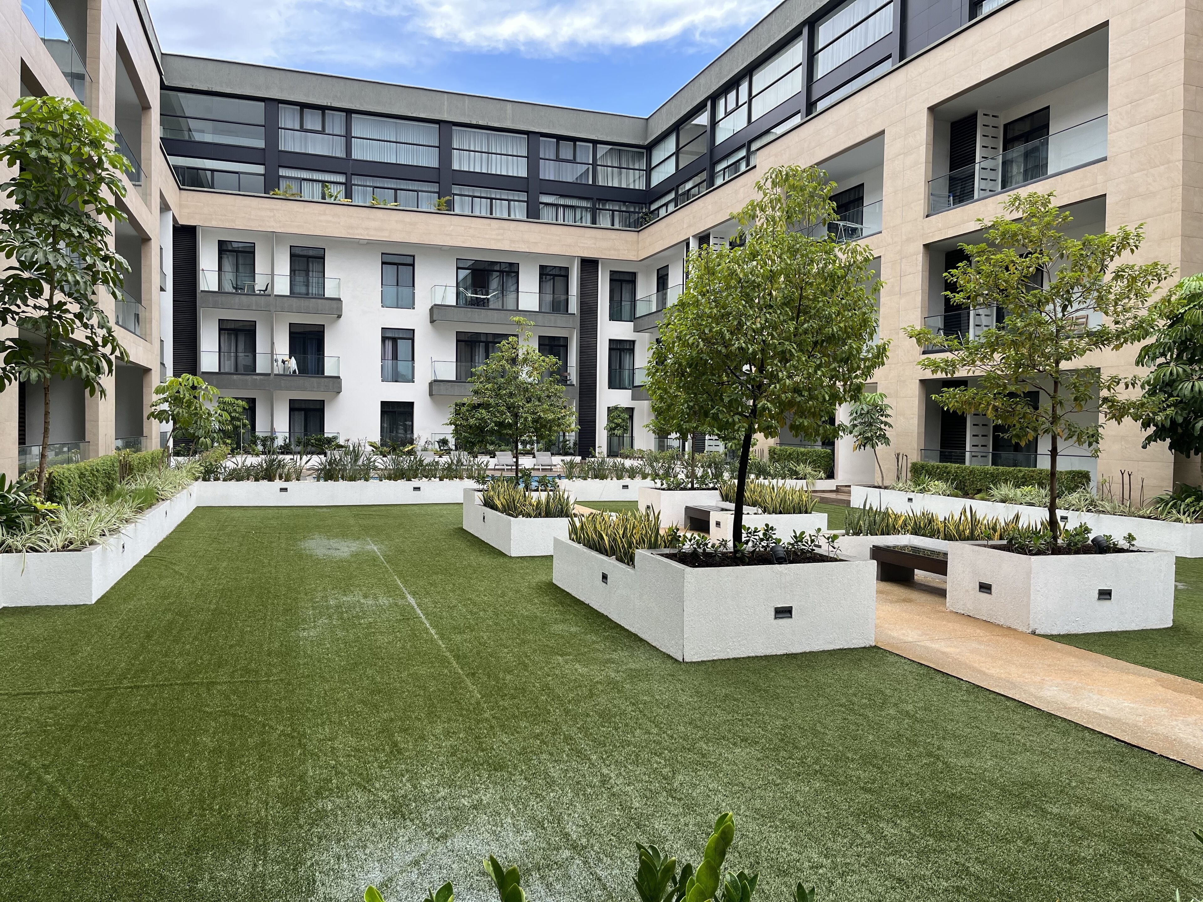 Un edificio moderno con varios balcones, un patio central con césped artificial y diversas plantas.