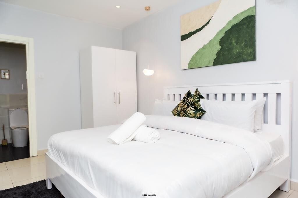 A modern bedroom with a white bed, a white wardrobe, and a painting on the wall.